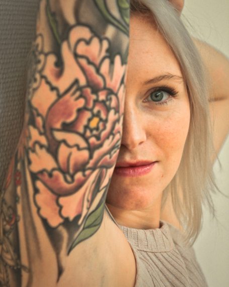 Portrait de femme Femme avec un tatouage coloré de pivoine sur le bras, regardant vers l'objectif.
