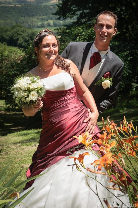Mariage-couple Une mariée en robe rouge et blanche avec un bouquet, posant avec un marié souriant.