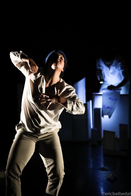 Spectacle - danse Danseur en mouvement sur scène, éclairage sombre avec des décors abstraits en arrière-plan.