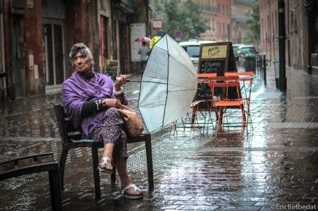 Femme sous la pluie Femme assise sur une chaise, abritée sous un parapluie, sous la pluie.