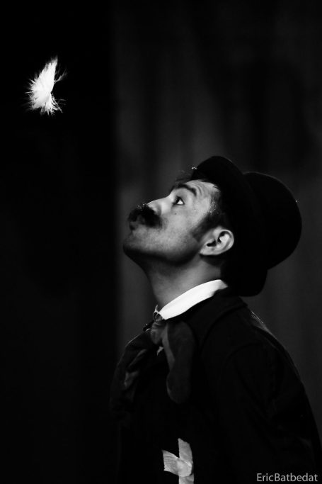 Spectacle de clown Un clown en costume avec moustache, regardant une plume blanche en vol.