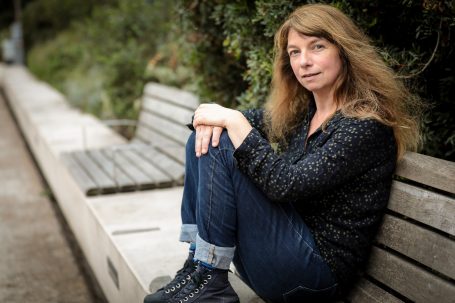 Book comédienne Femme assise sur un banc, regard pensif, cheveux longs et ondulés, vêtements décontractés.