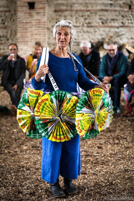Portrait de femme Femme souriante en tenue bleue portant des paniers colorés, entourée de personnes.